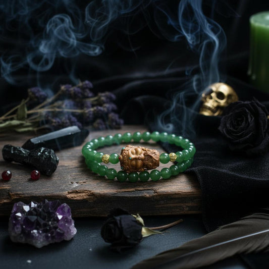 A close-up of a beaded bracelet worn on a wrist, featuring round green jade-like beads and a carved wooden Buddha head charm with small turquoise and red accents.