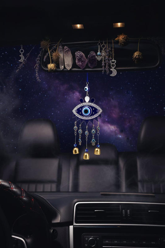 Car interior with an evil eye wind chime hanging from the rearview mirror, scenic road outside.
