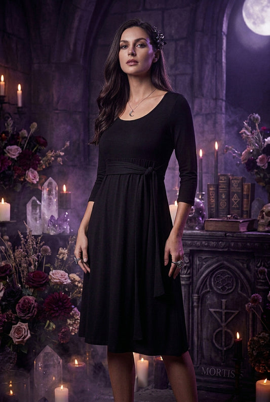 A woman wearing a black three-quarter sleeve dress with a scoop neckline and a matching fabric tie belt at the waist, shown against a plain white background.