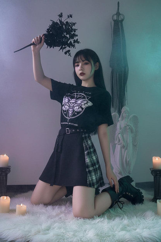 Person wearing a black t-shirt with a moth design and text, holding dark foliage, standing in front of a statue.