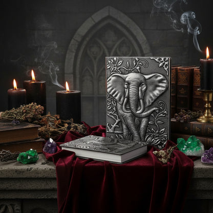 Two embossed elephant-themed notebooks or journals with a textured gray and silver finish, standing upright on a white surface with a clock and small plant in the background.