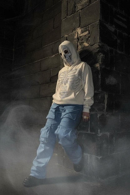 Person wearing a skeleton-themed hoodie and blue pants in an indoor setting with cars and pillars.
