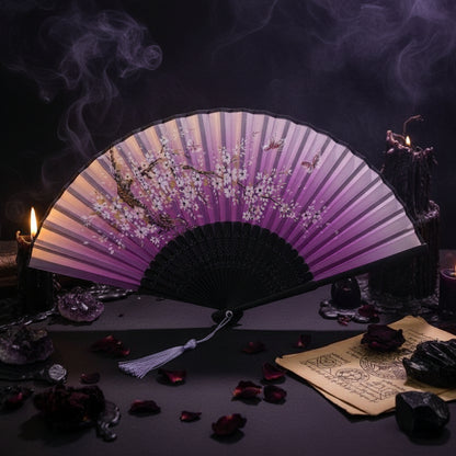 A traditional folding hand fan with a purple gradient design and white cherry blossom illustrations, featuring a black handle and tassel, styled with pink flowers on a white background.