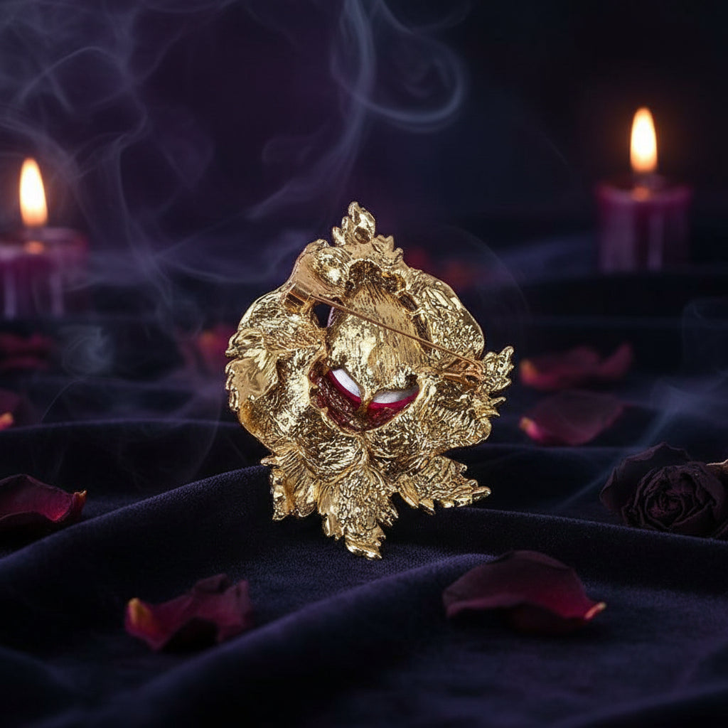 A gold-toned textured brooch featuring a central oval red gemstone, photographed on a plain light background.