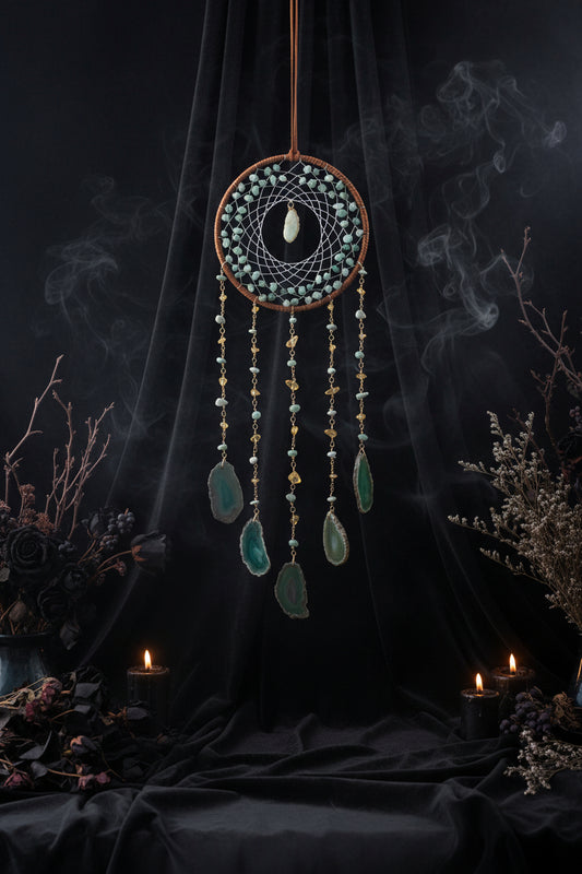 Decorative dreamcatcher with green stones and beads on a gray wall with flowers.