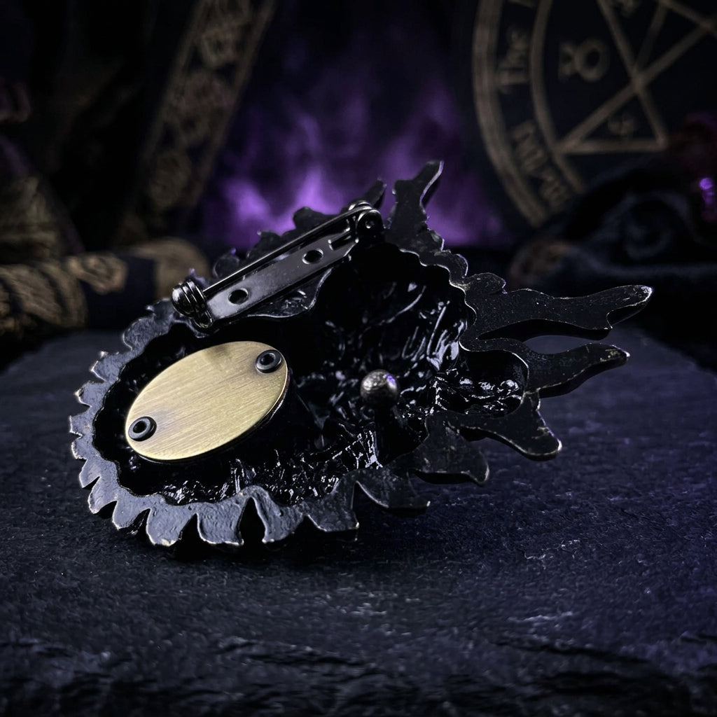 A black decorative belt buckle featuring a stylized skull or mask design with a metal spring ring, photographed on a plain white background.
