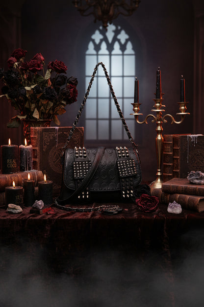 Black studded handbag on a white surface with a blurred background