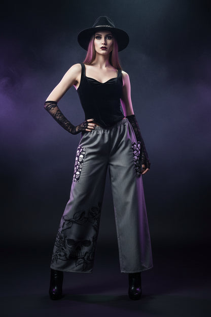 Gray wide-leg pants featuring a large black skull and rose graphic on one leg, plus black-and-white skull-patterned patch pockets on both legs.