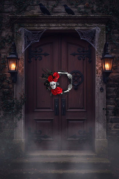 A gothic Halloween wreath decoration featuring a white skull, red artificial roses, black branches, and skeleton hands on a gray background.
