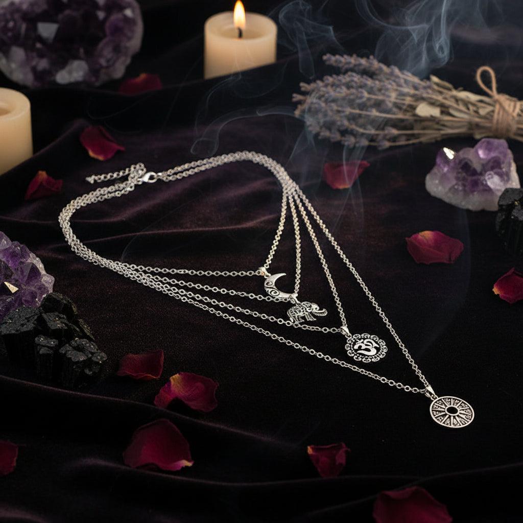 A layered silver necklace set with multiple delicate chains and pendants, including a crescent moon, a bird, a floral sun motif, and a circular medallion, displayed on a black background with a white printed card.