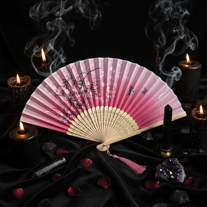 Pink and white folding fan with floral design on a light gray background with pink flowers.
