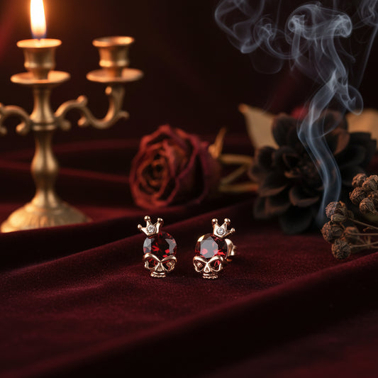 Skull-shaped earrings with red gemstones and gold accents on a white background