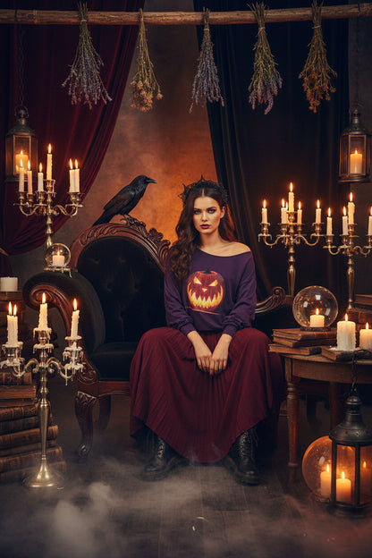 A purple off-the-shoulder long-sleeve sweatshirt featuring a large graphic print of a glowing jack-o'-lantern pumpkin on the front, set against a plain white background.