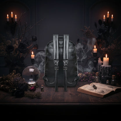 Black faux leather backpack shown from the back, featuring dual padded shoulder straps with metal buckle adjusters, a top carry handle, and side compression straps, set against a plain white background.