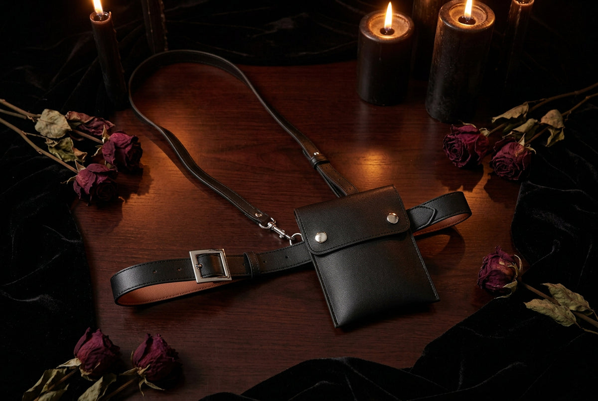 Black leather waist bag on a light gray surface with a pen, paper, and perfume bottle.
