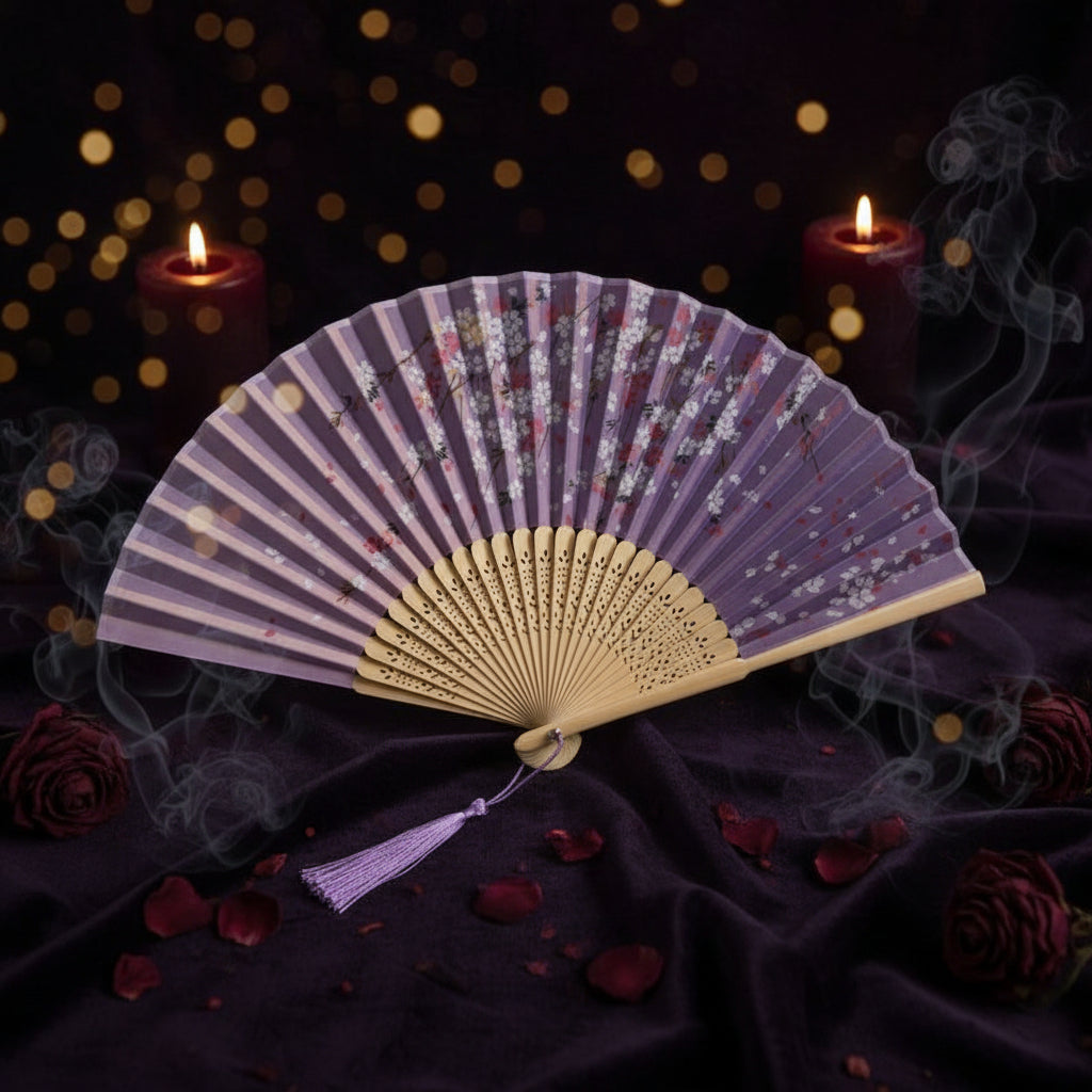 A traditional folding hand fan with a lavender and white floral pattern, a beige wooden handle, and a purple tassel, styled with pink cherry blossoms on a white background.