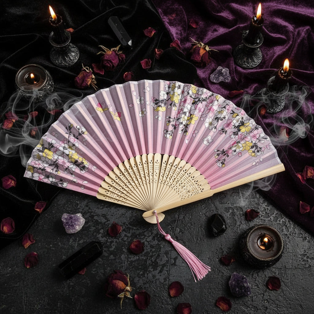 Pink floral folding fan with tassel on a light pink background with flowers.