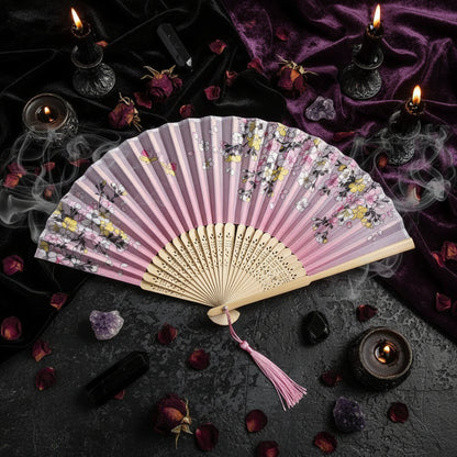 Pink floral folding fan with tassel on a light pink background with flowers.