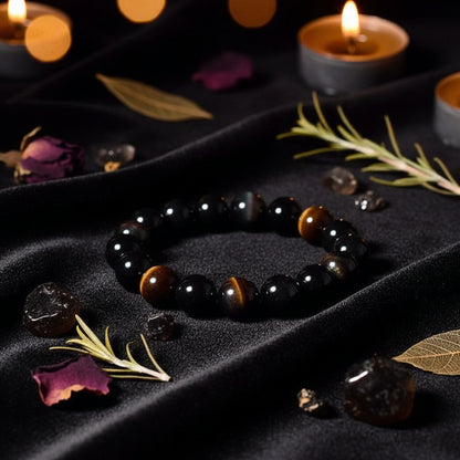 A beaded bracelet made of glossy black gemstone beads with a small gold and brown decorative accent, arranged on a textured dark surface with a piece of wood.