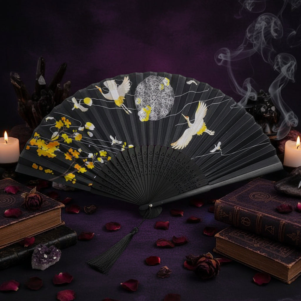 Black hand fan with white storks and yellow flowers on a white surface.