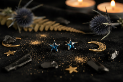 A pair of silver star-shaped stud earrings with blue faceted gemstones, displayed on a neutral light gray surface.
