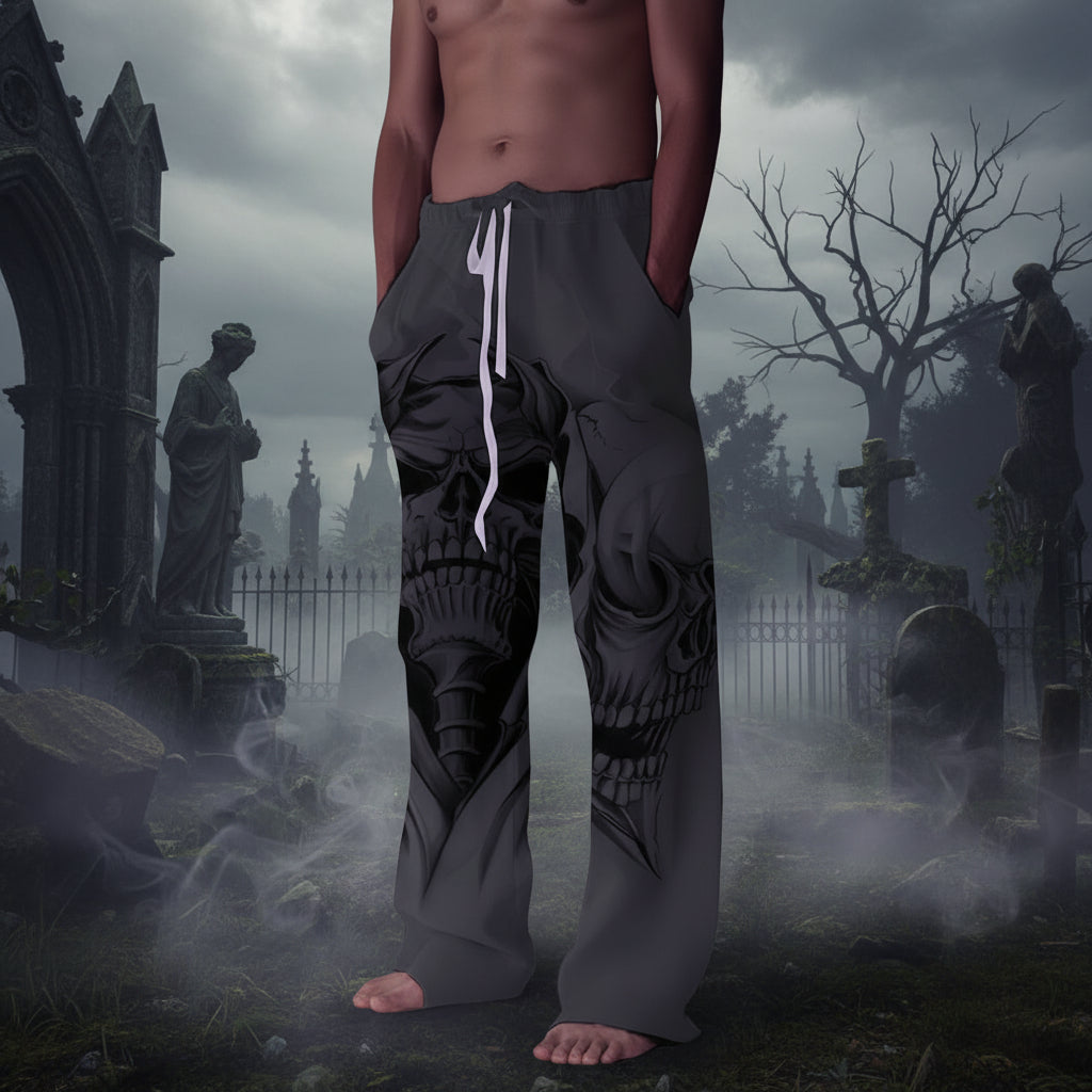 A person wearing loose gray drawstring pants with a large black skull graphic printed across the front, standing barefoot against a plain light gray wall.