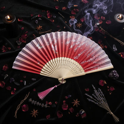 A traditional folding hand fan with a red and pink gradient design and white floral patterns, displayed on a white background with pink cherry blossom flowers.