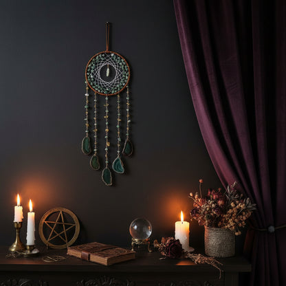 Decorative dreamcatcher with green stones on a white wall with books and a plant.