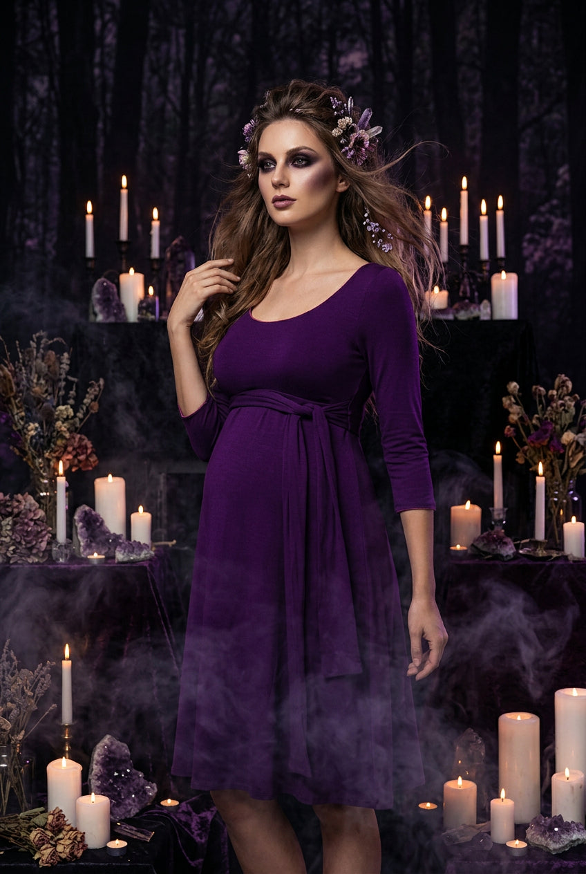 A woman wearing a purple three-quarter sleeve dress with a scoop neckline and a matching fabric tie belt at the waist, shown against a plain white background.