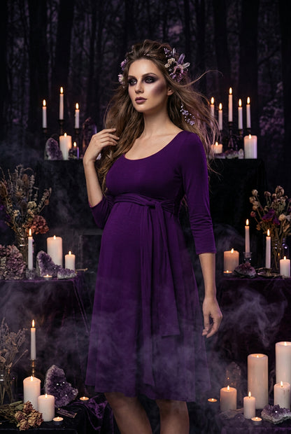 A woman wearing a purple three-quarter sleeve dress with a scoop neckline and a matching fabric tie belt at the waist, shown against a plain white background.