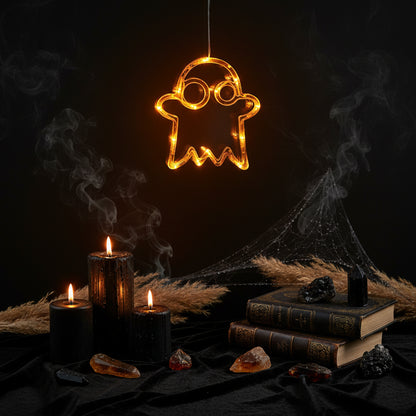 A glowing orange ghost-shaped LED light hanging on a window, with a dark blurred indoor background and a small label in the top left that reads 'D-Ghost'.