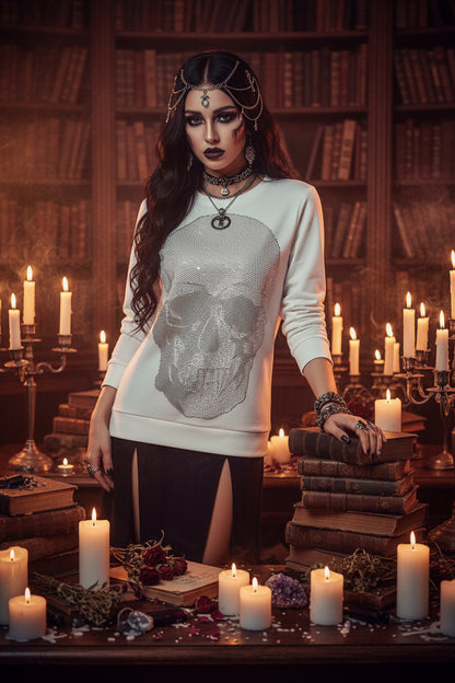 A white crewneck sweatshirt with a large skull graphic embellished with sparkling rhinestones, hanging on a black hanger against a dark gray background.