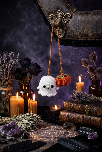 A pair of crocheted car air fresheners hanging from the rearview mirror inside a car. One is a white ghost with black embroidered eyes and mouth, and the other is an orange pumpkin with a green stem.