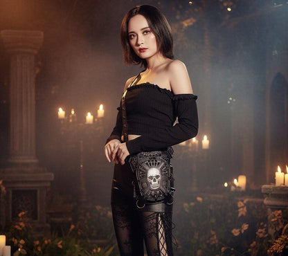 A fashion model shot featuring a black off-the-shoulder long-sleeve crop top and a black lace skirt with a skull-patterned bag, posed against a dark background with a red railing.