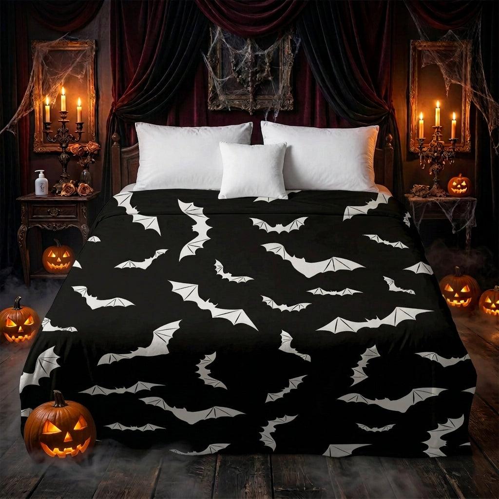 A bed dressed in a black blanket or sheet featuring an allover white bat print, styled in a bedroom with gray and white pillows, a wooden side table, and a woven pouf.