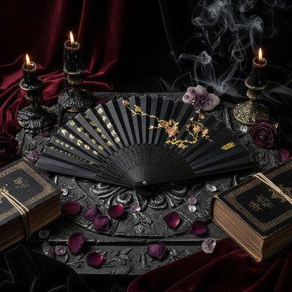 Black folding fan with floral designs on a white surface with pink flowers.
