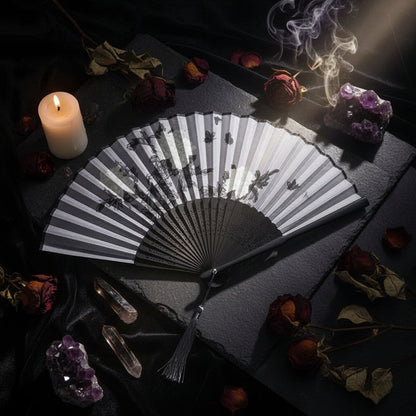 Black and white folding fan with floral design on a light pink background with pink flowers.