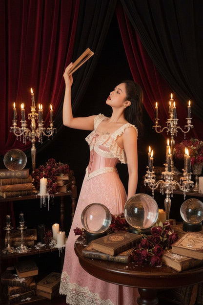 Woman in a pink lace dress sitting on a patterned couch with decorative frames in the background.