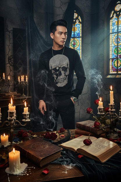 A man wearing a black long-sleeve crewneck sweater with a large, eye-catching skull graphic embellished with sparkling silver rhinestones on the front. The photo is cropped from the neck down, showing the model wearing black pants, a silver necklace, and a green-accented watch.