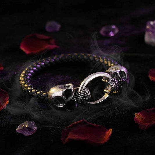 A black braided leather bracelet with a silver-toned skull ring clasp, displayed on a dark textured background.