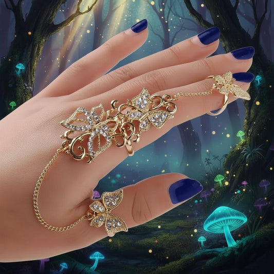 Gold butterfly ring set with clear crystals, shown worn on a hand with dark red and gold manicured nails against a plain white background.