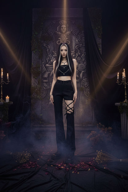 A model wearing a black sleeveless crop top and black high-waisted distressed flare jeans with lace-up detailing on the lower leg, paired with black platform shoes, standing against a textured gray concrete wall.
