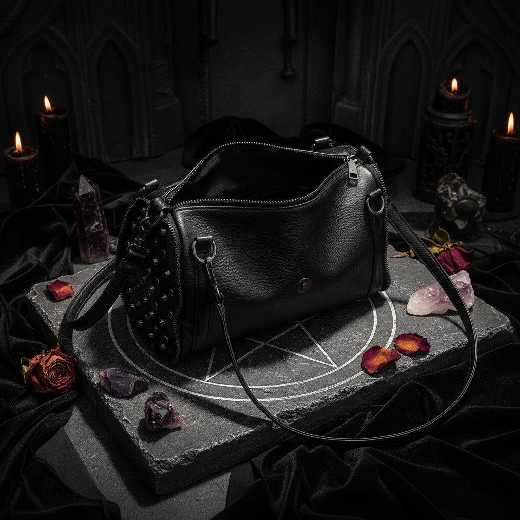 A black pebbled leather shoulder bag with a studded front pocket and silver-tone hardware, shown open on a white table.