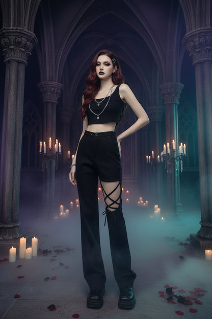 A model wearing a black sleeveless crop top with silver chain details and black high-waisted pants featuring a leg cutout with crisscross straps, standing against a textured gray wall.