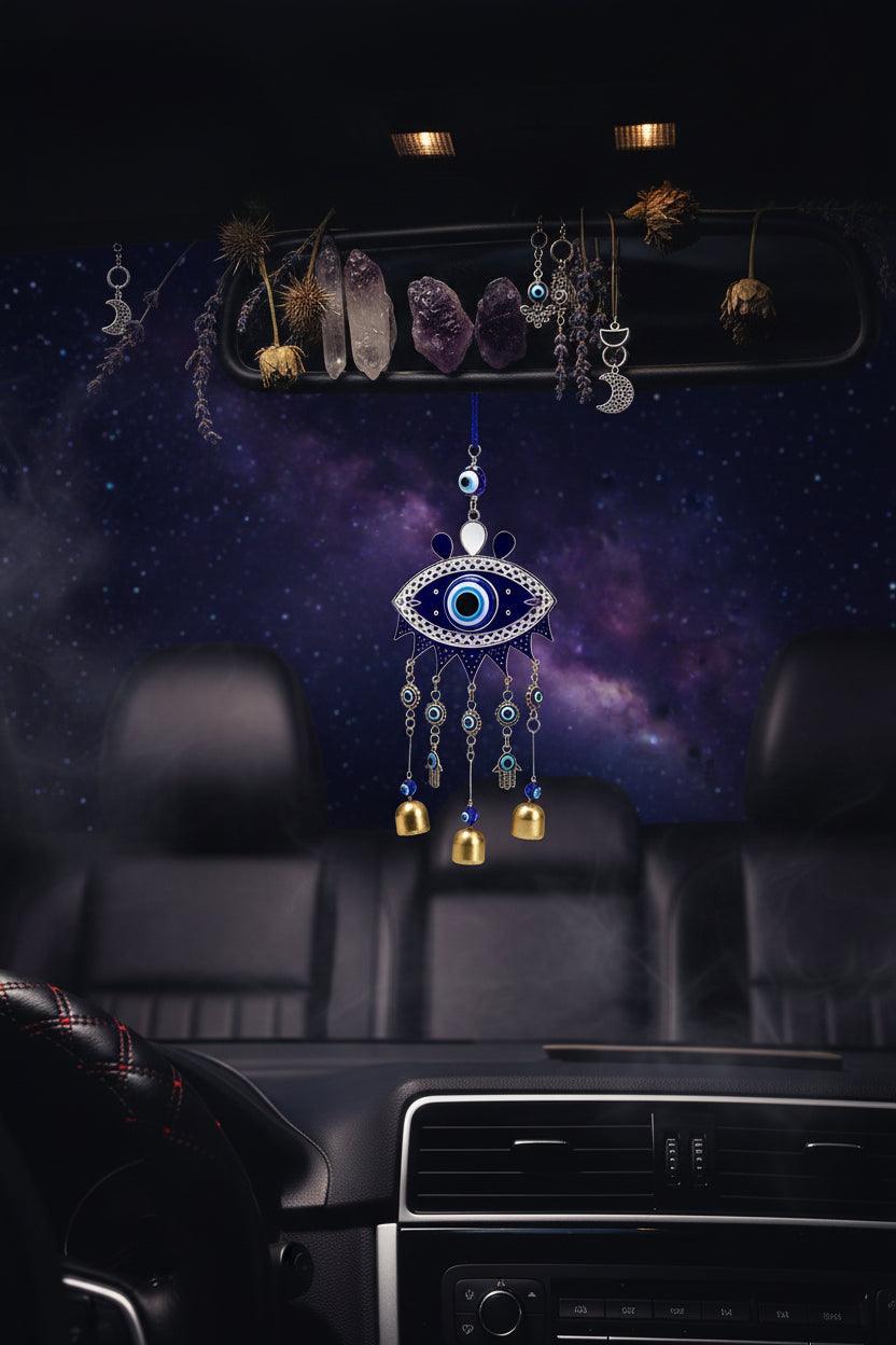 Car interior with an evil eye wind chime hanging from the rearview mirror, scenic road outside.