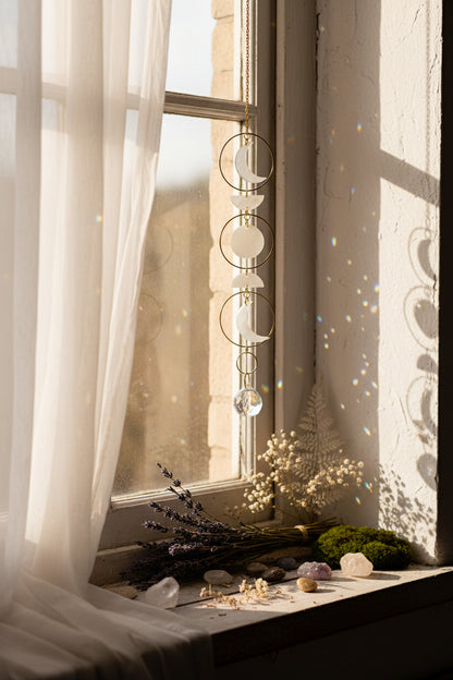 Decorative hanging with moon phases and gold chain on a textured wall background