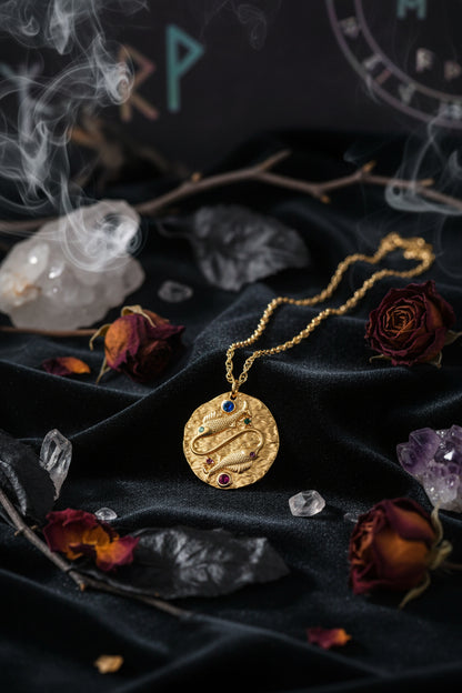 Gold necklace with a circular pendant featuring gemstones on a white background