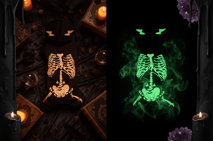 A black plush pet hoodie shown from the back, featuring a skeleton graphic. The left side shows the design in normal light as white, while the right side shows it glowing green in the dark.