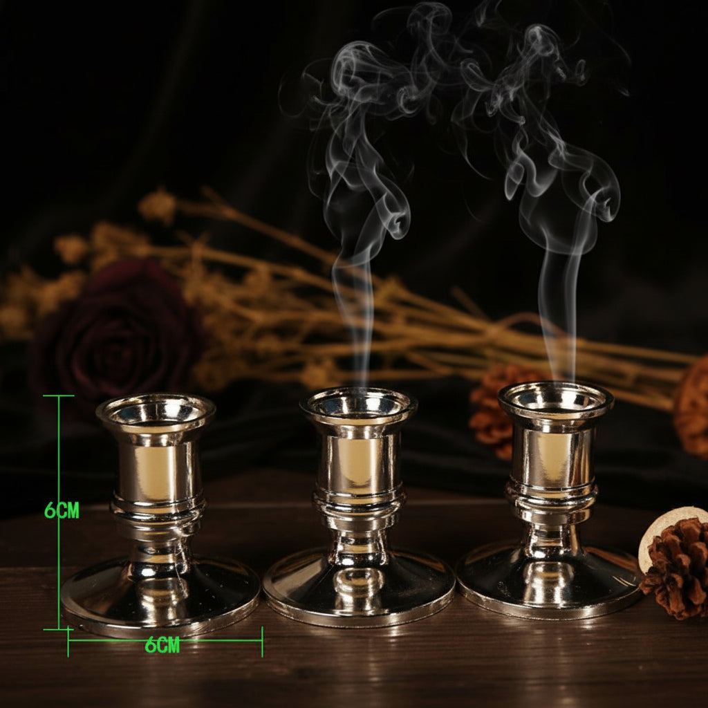 Three metallic candle holders on a wooden surface with a blurred background of a cup and woven basket.