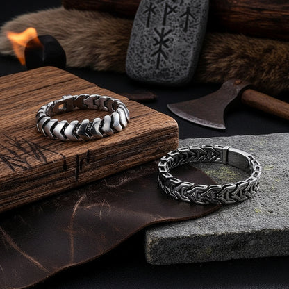 Two silver-toned chunky chain-link bracelets displayed on a dark textured surface, with one bracelet resting on a black box and the other placed below it.